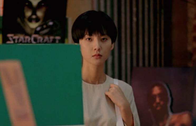 Yum Jung-ah sentada numa sala com um pôster de StarCraft ao fundo